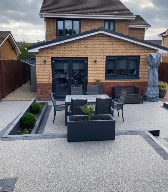 Grey resin bound terrace with garden furniture beside a rendered house